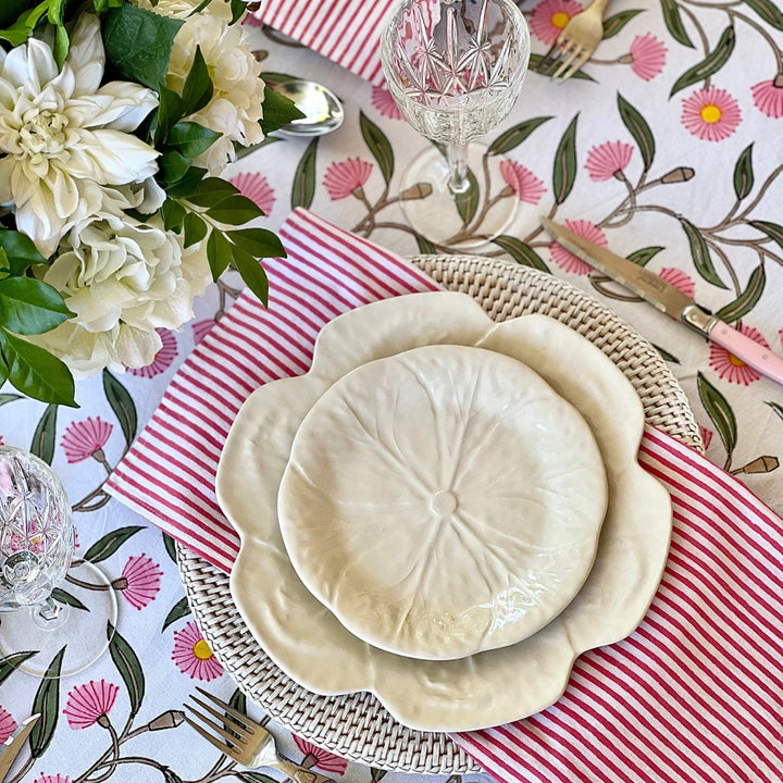 A set of four white and pink striped table napkins  placed on a table with a hand block printed floral patterned tablecloth and cutlery.