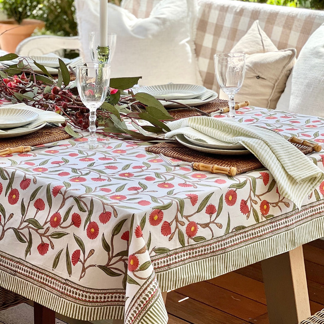 A square hand block printed tablecloth with a red flowering gum design displayed on a table outdoors.