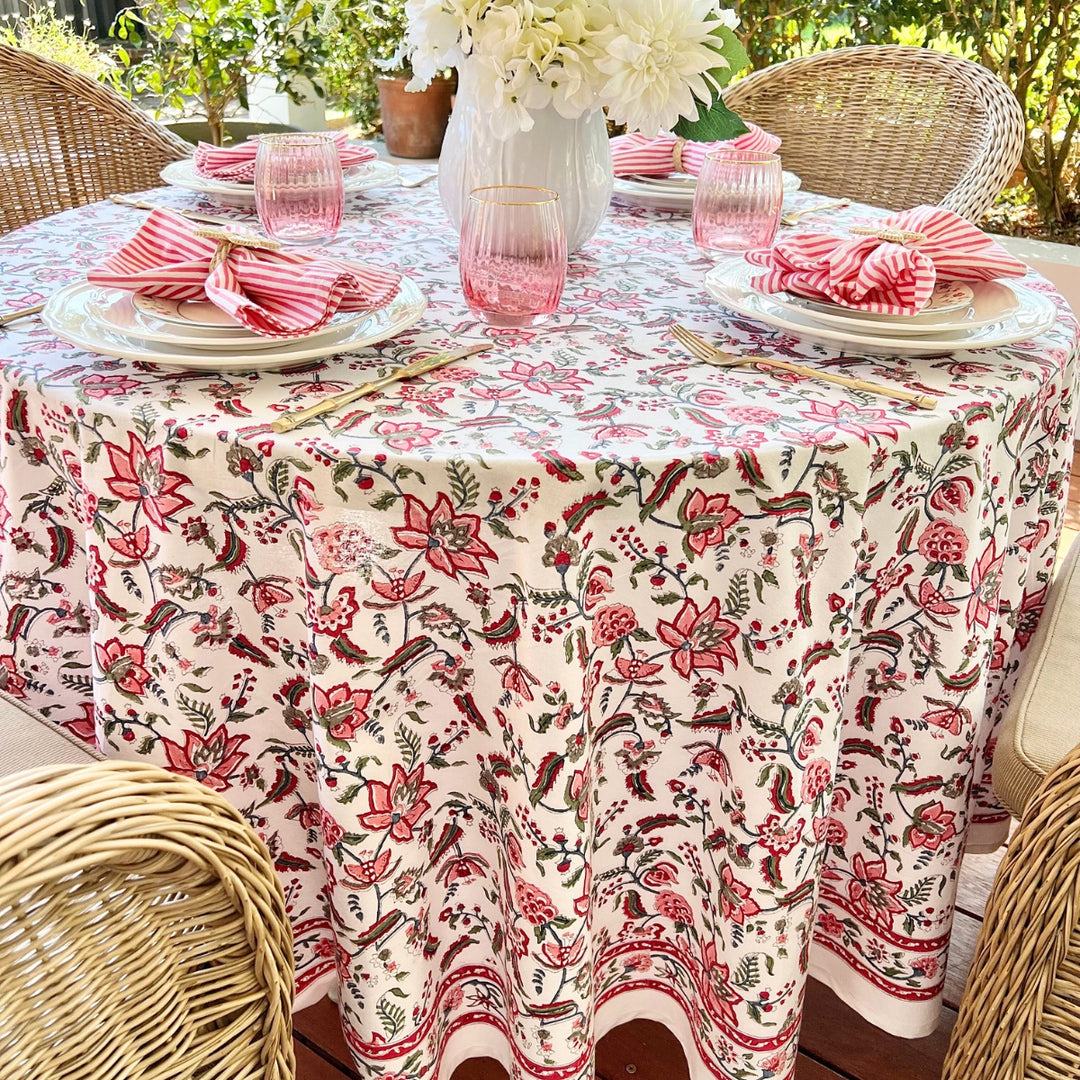 A multicolored round tablecloth with a pattern of hand block printed pomegranates and green leaves, displayed on a table set with plates and glasses.