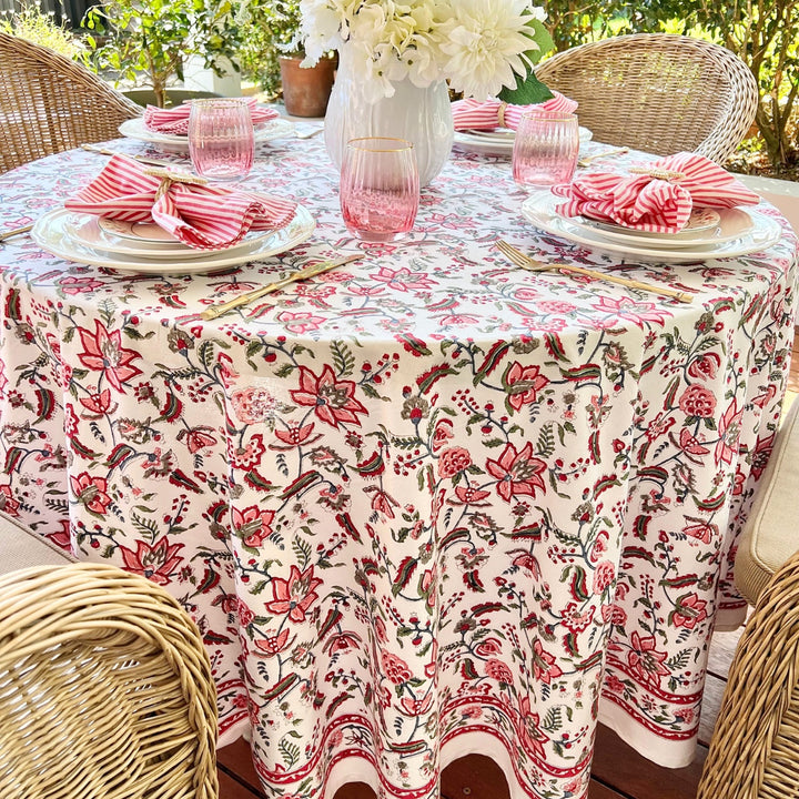 A multicolored round tablecloth with a pattern of hand block printed pomegranates and green leaves, displayed on a table set with plates and glasses.
