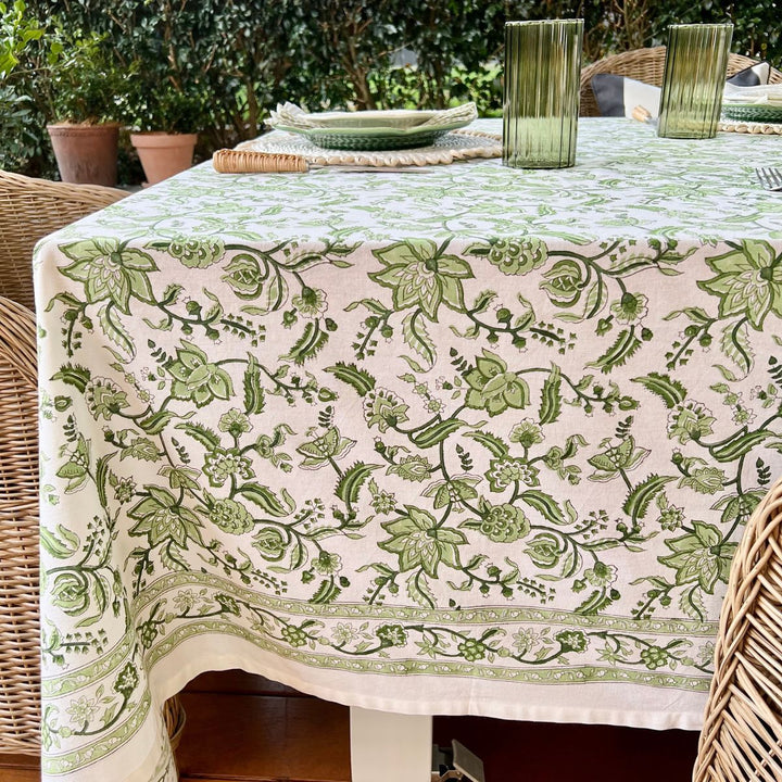 A green and white hand block printed chintz patterned square tablecloth displayed over a wicker table.