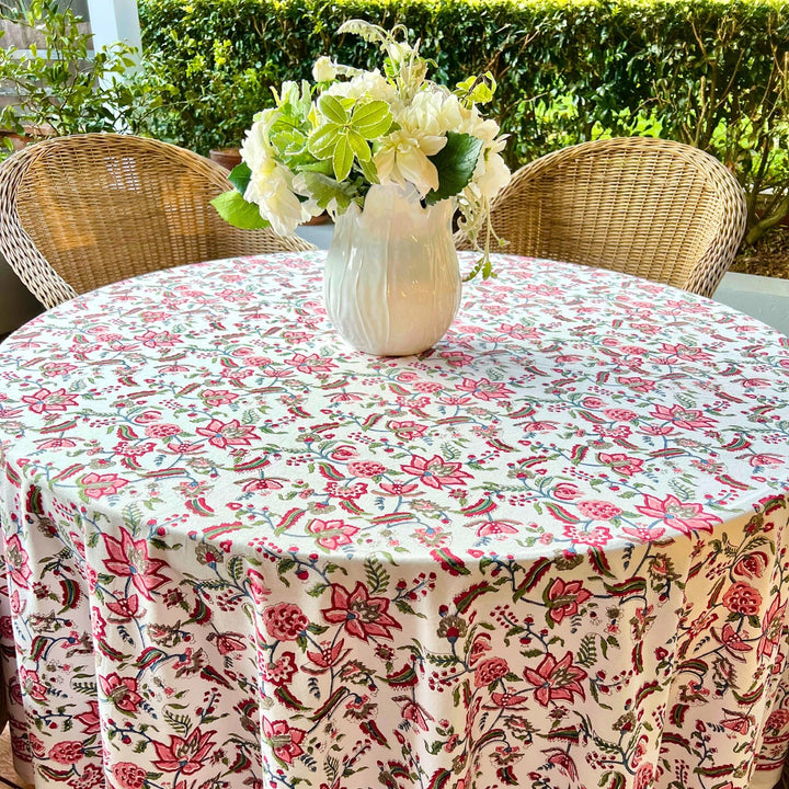 A multicolored round tablecloth with a floral pattern, featuring bold red hand-painted pomegranates and vibrant green leaves, displayed on a table.