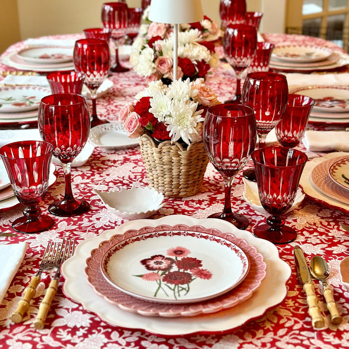 Decorative table setting with red glasses, floral plates, and a red and white patterned tablecloth.