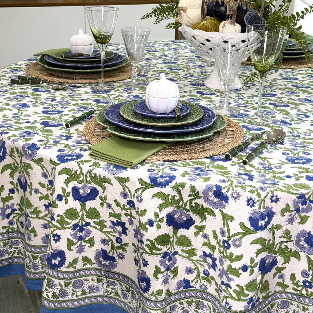Blue and green floral circular table cover with a patterned border draping over a round dining table set for a fall dinner