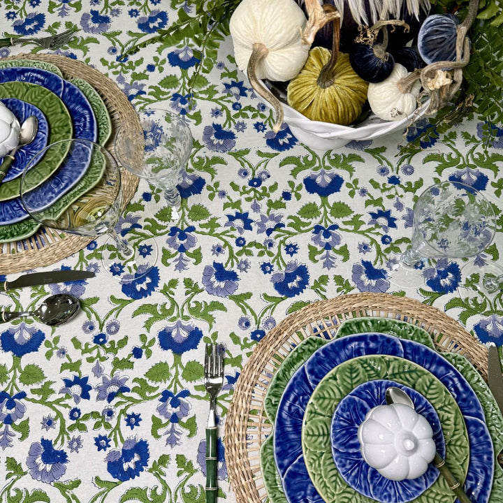 Overhead view of a blue and green floral tablecloth styled with festive dinner plates, white pumpkins, and seasonal gourds for Thanksgiving dinner.