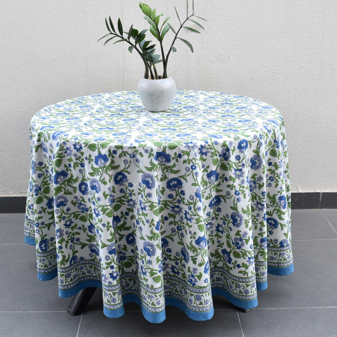 Round hand block printed cotton tablecloth in blue and green floral pattern draped over a round table with a potted plant