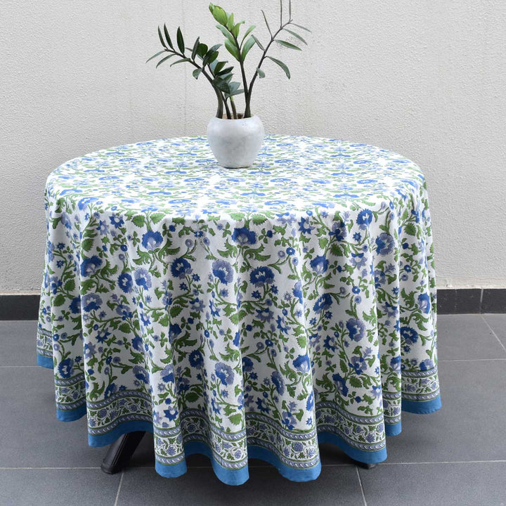 Round hand block printed cotton tablecloth in blue and green floral pattern draped over a round table with a potted plant