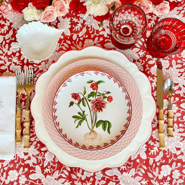 An overhead view of a Christmas table setting with a floral dish on a red white floral Block printed table cloth