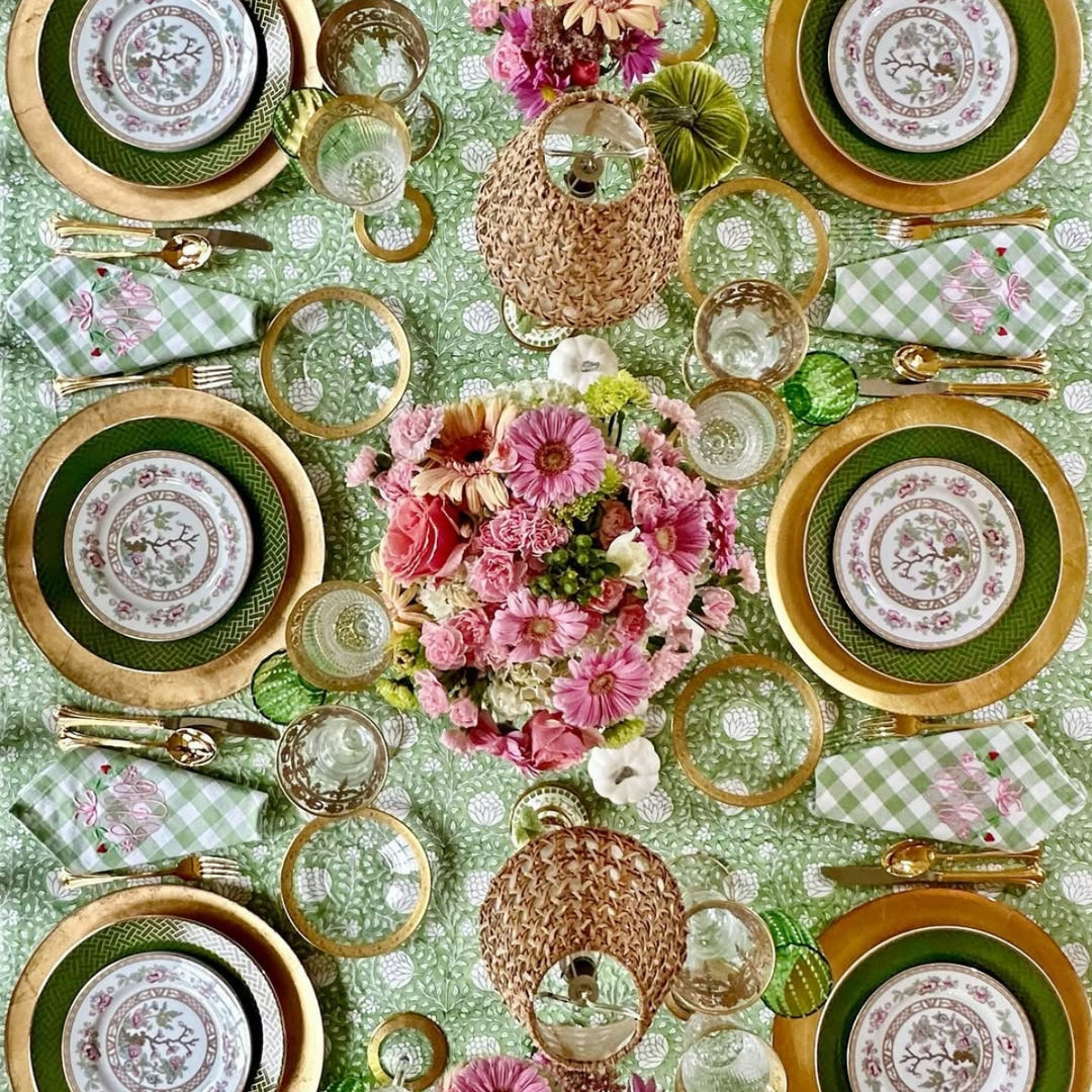 A rectangular hand block printed Eden tablecloth in green and white, set for Thanksgiving with a centrepiece of mini pumpkinsand autumnal foliage. green check napkins folded  with copper cutlery at each place setting.