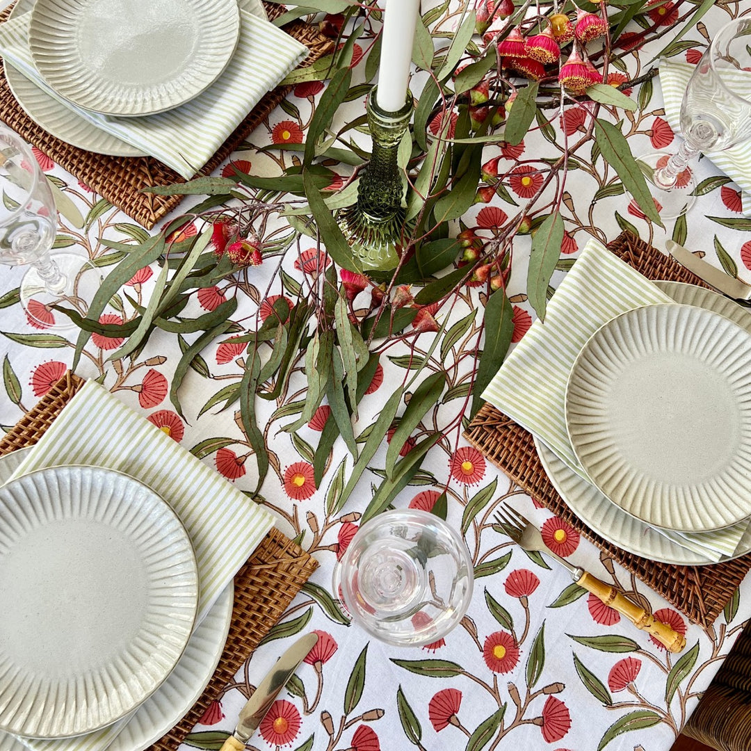 A large rectangular table featuring green striped cotton napkins and red green cotton floral tablecloth with flowering gums
