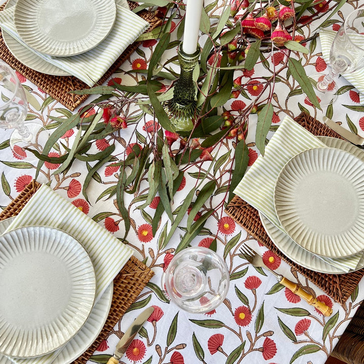 A large rectangular table featuring green striped cotton napkins and red green cotton floral tablecloth with flowering gums
