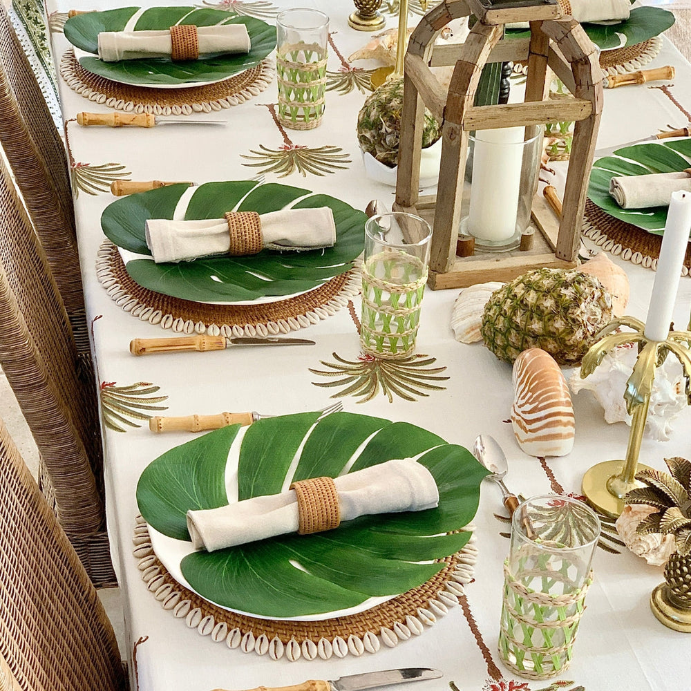 A tropical table on a square green palm hand block printed tablecloth with intricate floral border.