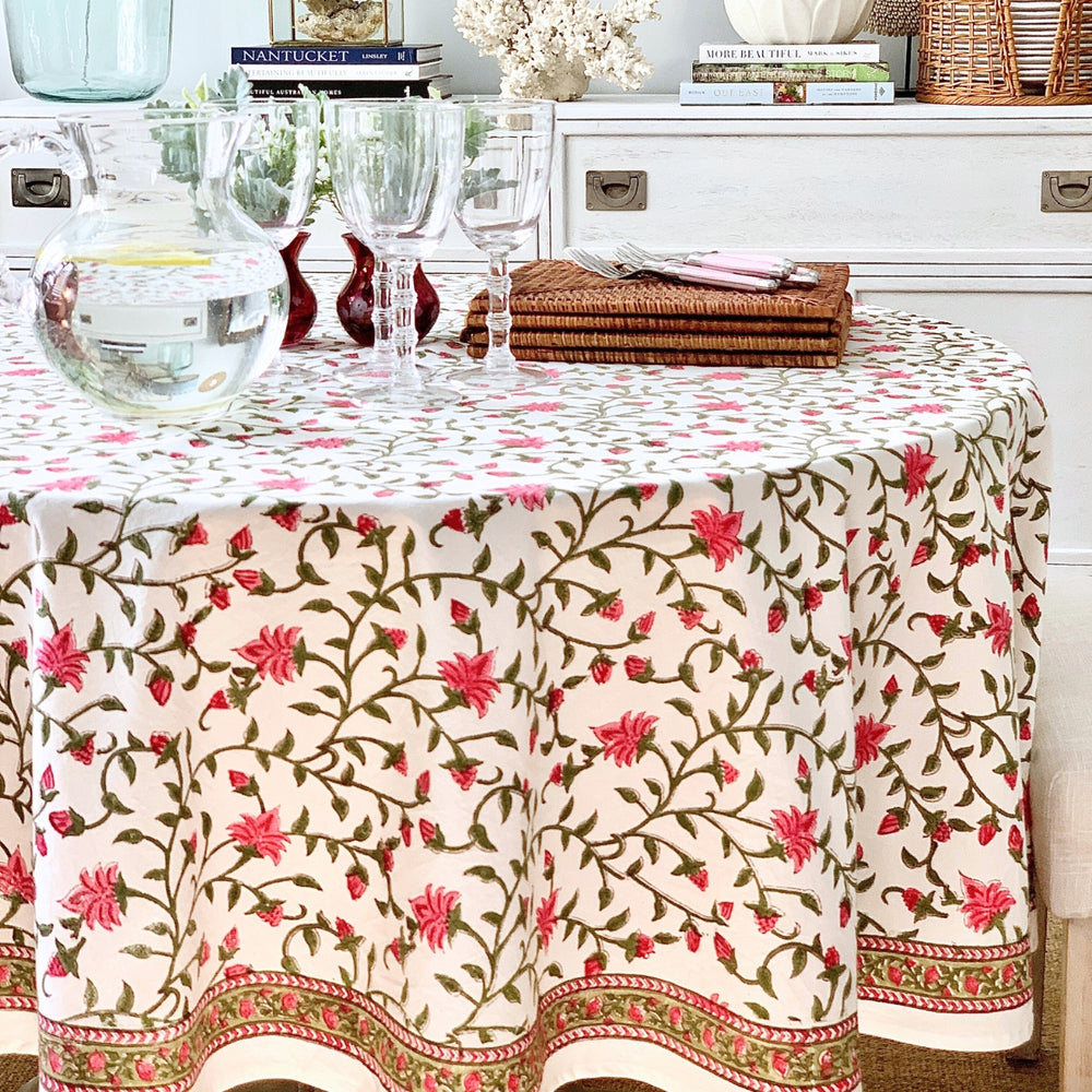 A circular hand block print table cover with a pink floral pattern and green vines.