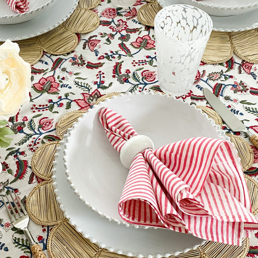 Pink cotton large napkins on white dish on a vibrant floral tablecloth