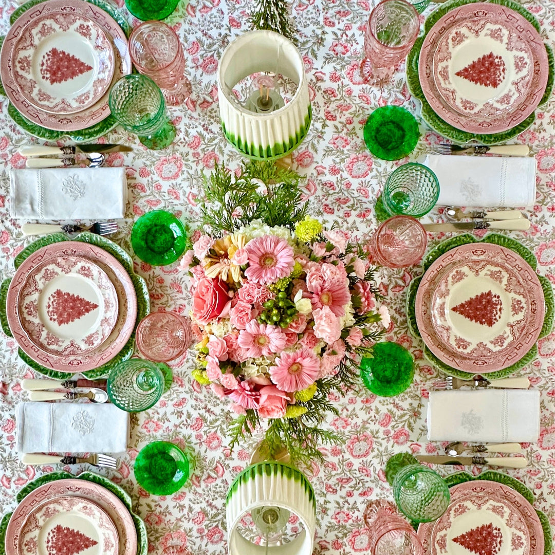 Top-down view of a square pink and green block printed tablecloth on a  wooden table, styled with festive  crockery and fresh florals for a.Christmas brunch table.