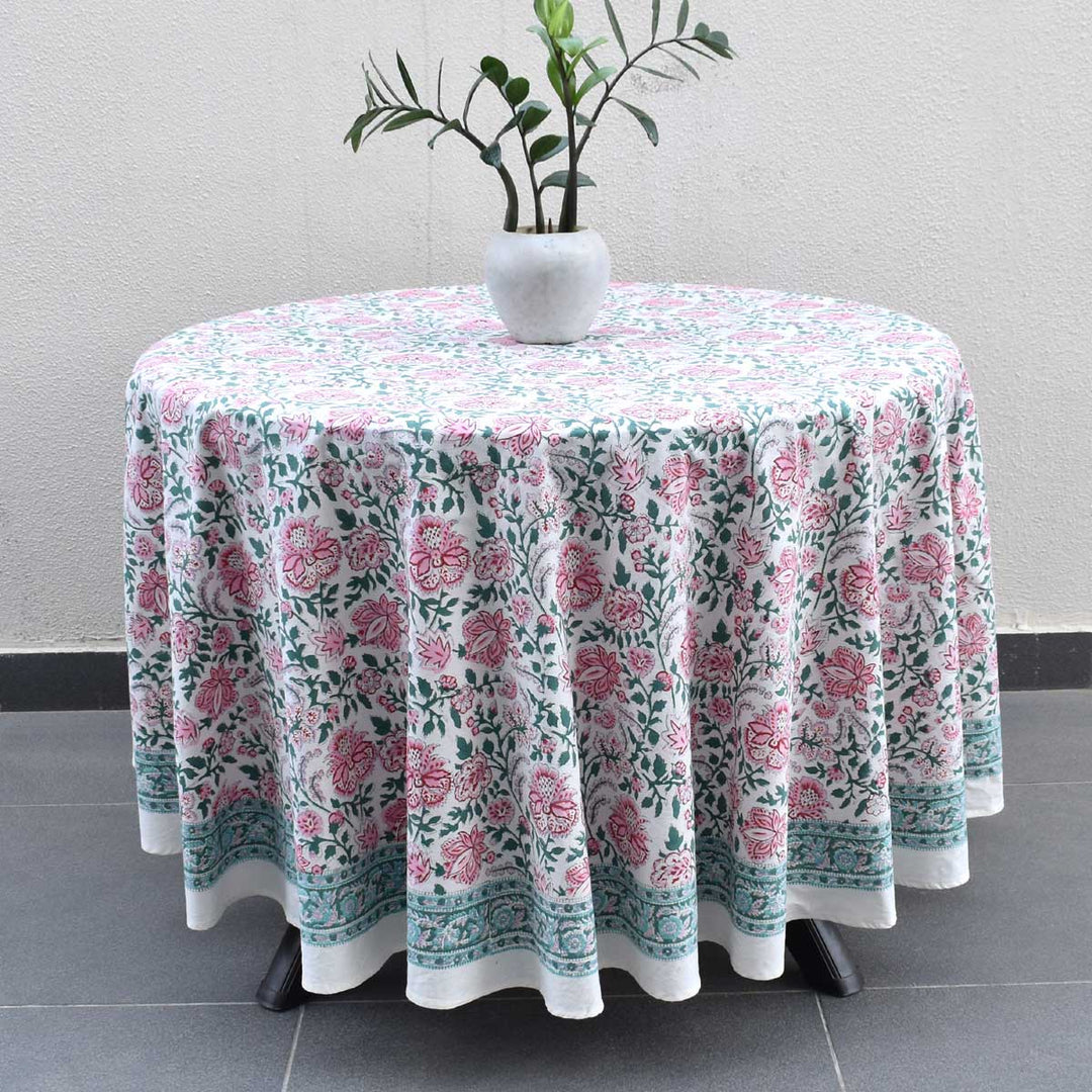 Hand block printed floral pattern in Pink green and blue colors on a round tablelcoth laid flat on a wooden round table for a casual brunch