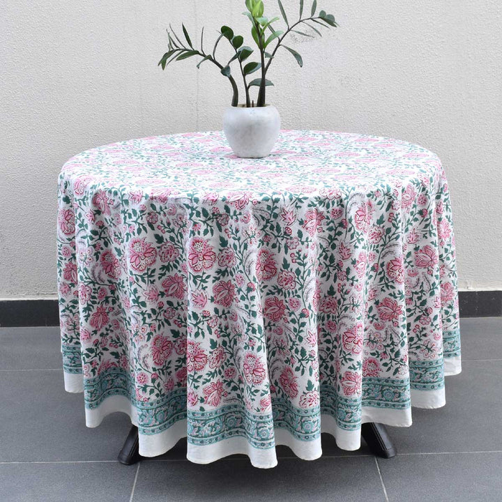Hand block printed floral pattern in Pink green and blue colors on a round tablelcoth laid flat on a wooden round table for a casual brunch