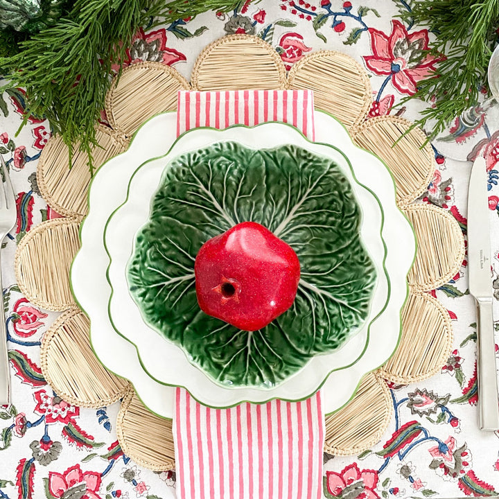 Pink striped cotton napkin  folded and laid under a green cabbageware bowla nd red ceramic pomegrante with green foilage for christmas setting