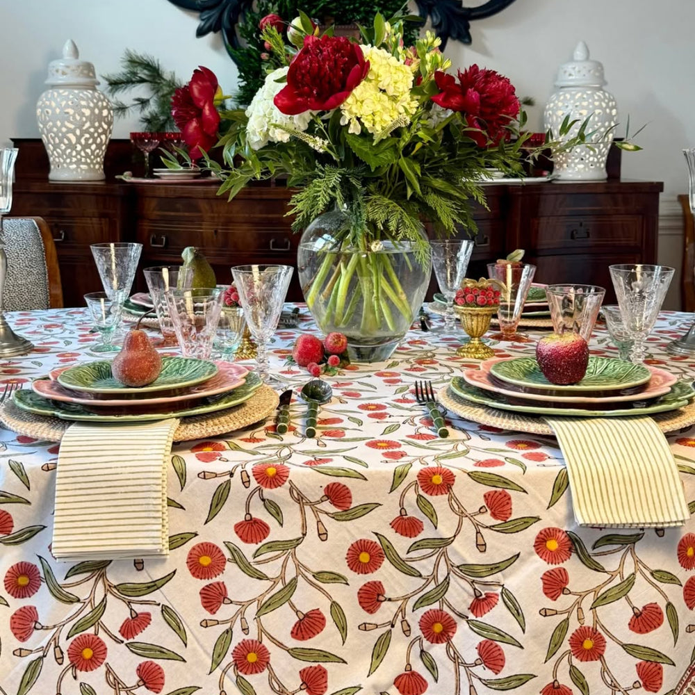 Red Flowering Gums hand block printed tablecloth set for a holiday dinner on a large table for six, with green striped napkins folded, beaded frui and a centrepiece of florals in a glass vase.