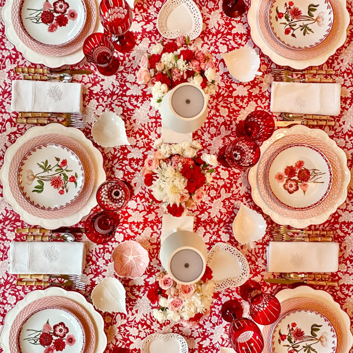 Decorative table setting with floral plates , red glasses, floral centrepieces and red christmas tablecloth 