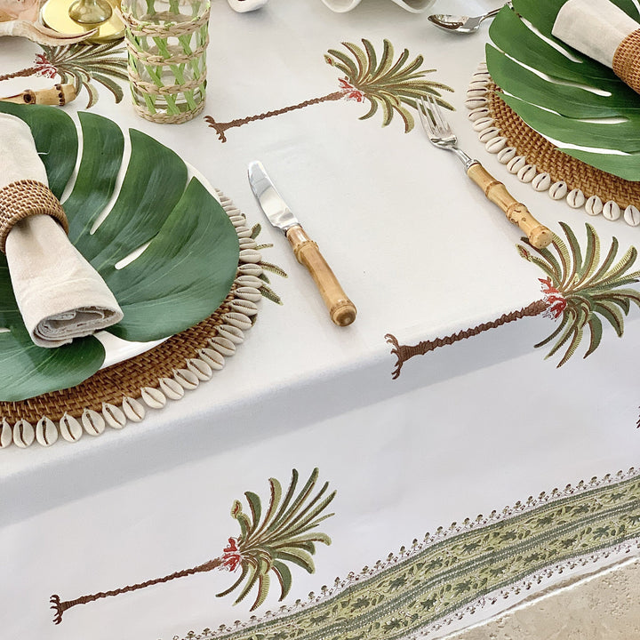 Tropical-themed table setting with palm leaf on white plates and decorative palm tree elements.
