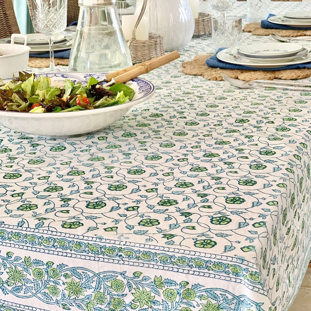 blue and green block print floral tablecloth displayed on a large rectangular tablecloth with salad, glass jugs and white dishes for casual dining