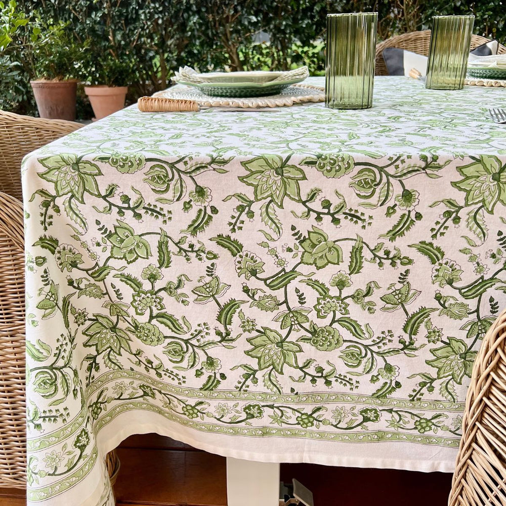 A green and white hand block printed chintz patterned square tablecloth displayed over a wood table.