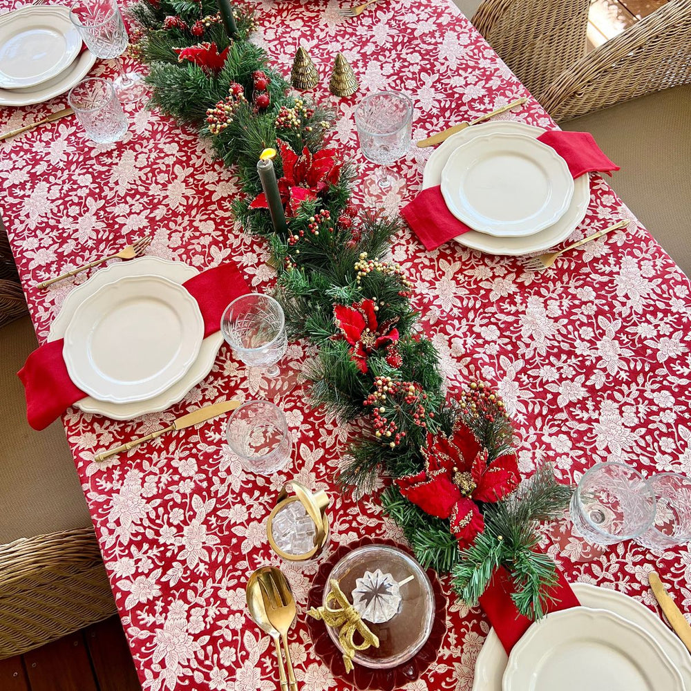 red and white tablecloth in a Christmas setting displayed over a large wooden table with greenery and Christmas ornaments