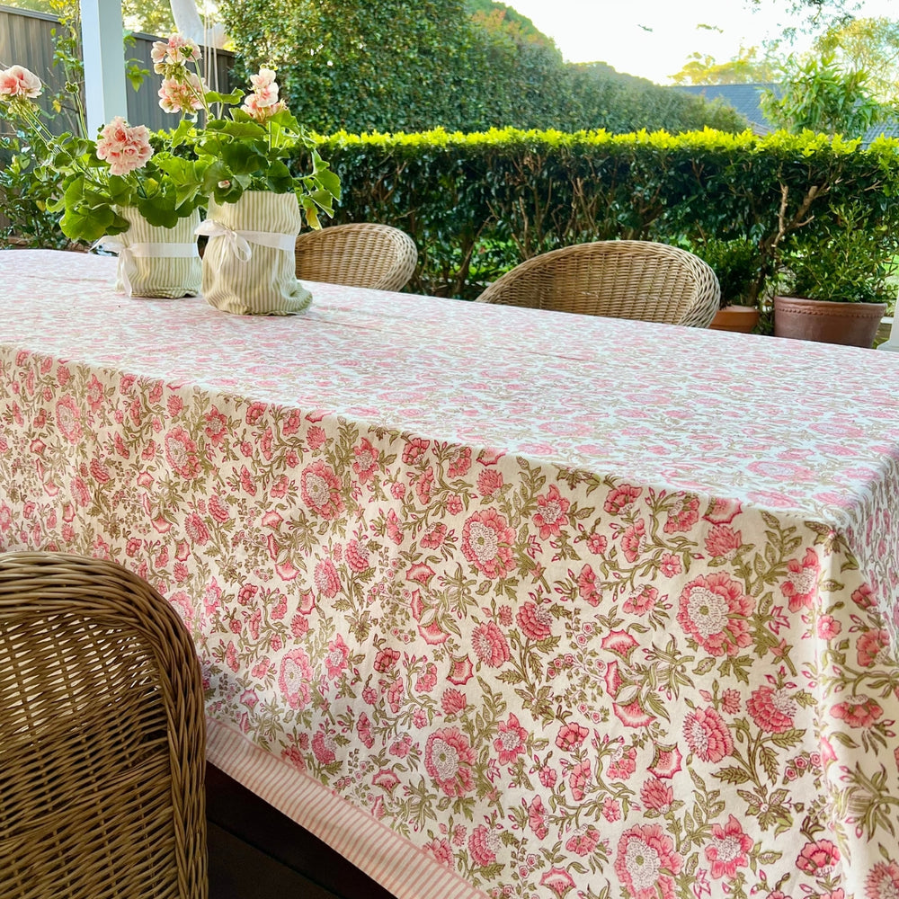 A rectangular hand block printed tablecloth in pink and green floral patterns, draped over a long dining table set with ceramic plates and linen napkins.