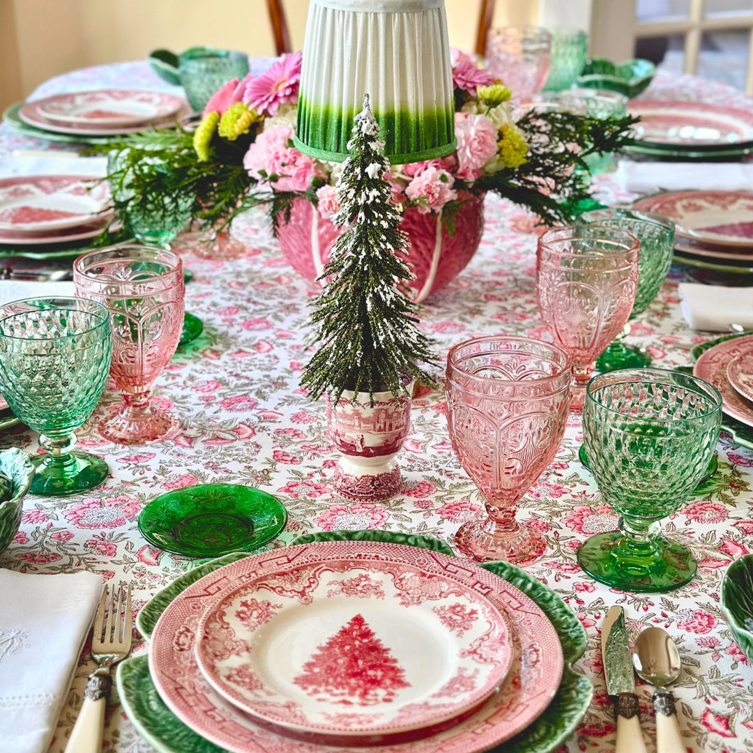 Decorative Christmas table setting with floral centerpieces, colorful glassware, and red and green plates.