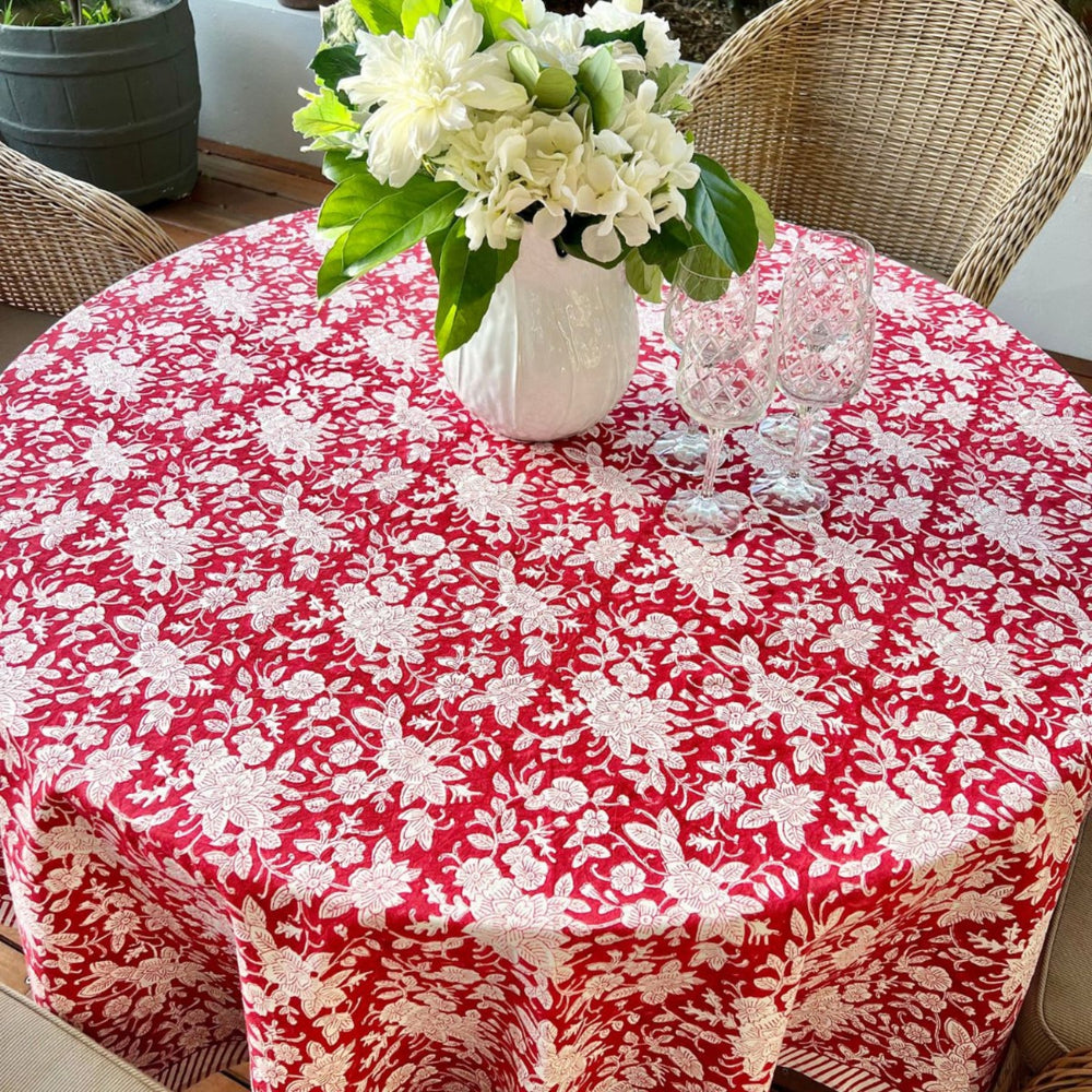 A hand block printed round tablecloth in red and white colors laid out on a circular table in alfresco setting with wicker chairs.