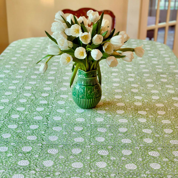Close-up of a rectangular Eden tablecloth corner showing the hand block printed green and white floral on a large table
