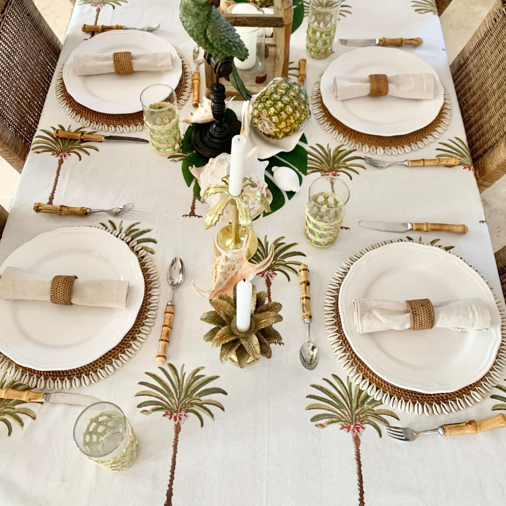 A large rectangle tablecloth with a green palm tree pattern displayed on a dining table set with dishes and decorative items.